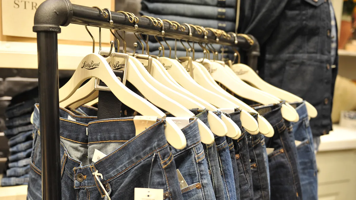 Denim jeans hang on wooden hangers on a metal rack.