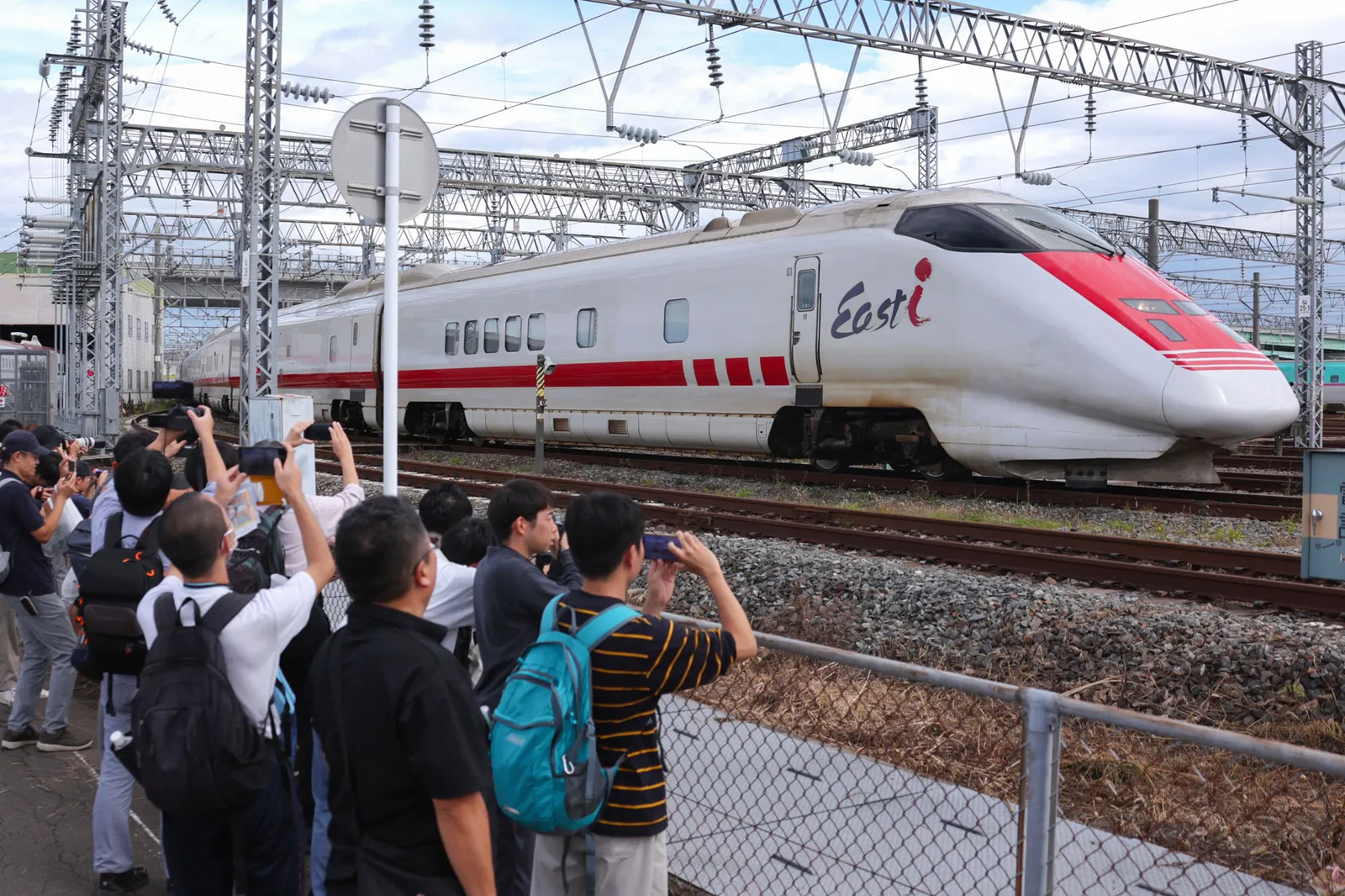 People with cameras watching a white and read bullet train.