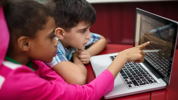 Two young students look at a computer together as one points at the screen.