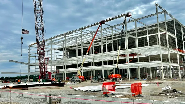 The steel structure of a building is exposed to the elements while construction equipment litters the photo around it.