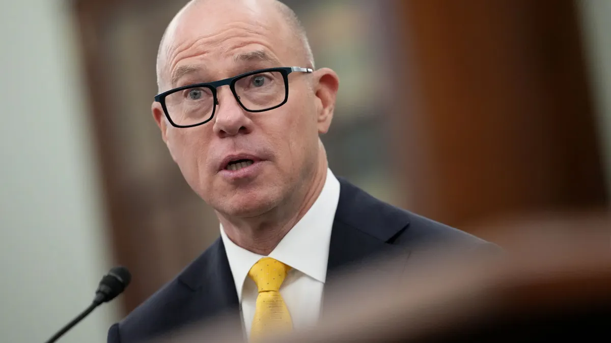 A man with glasses and a suit speaking into a microphone.