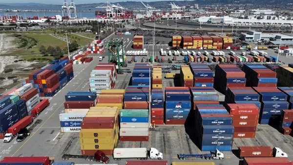 In an aerial view, trucks drive by shipping containers at the Port of Oakland