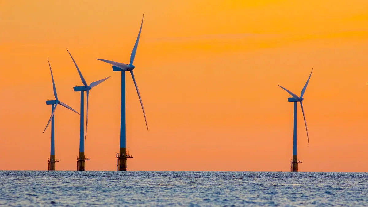 Offshore wind farm energy turbines at dawn against an orange sky