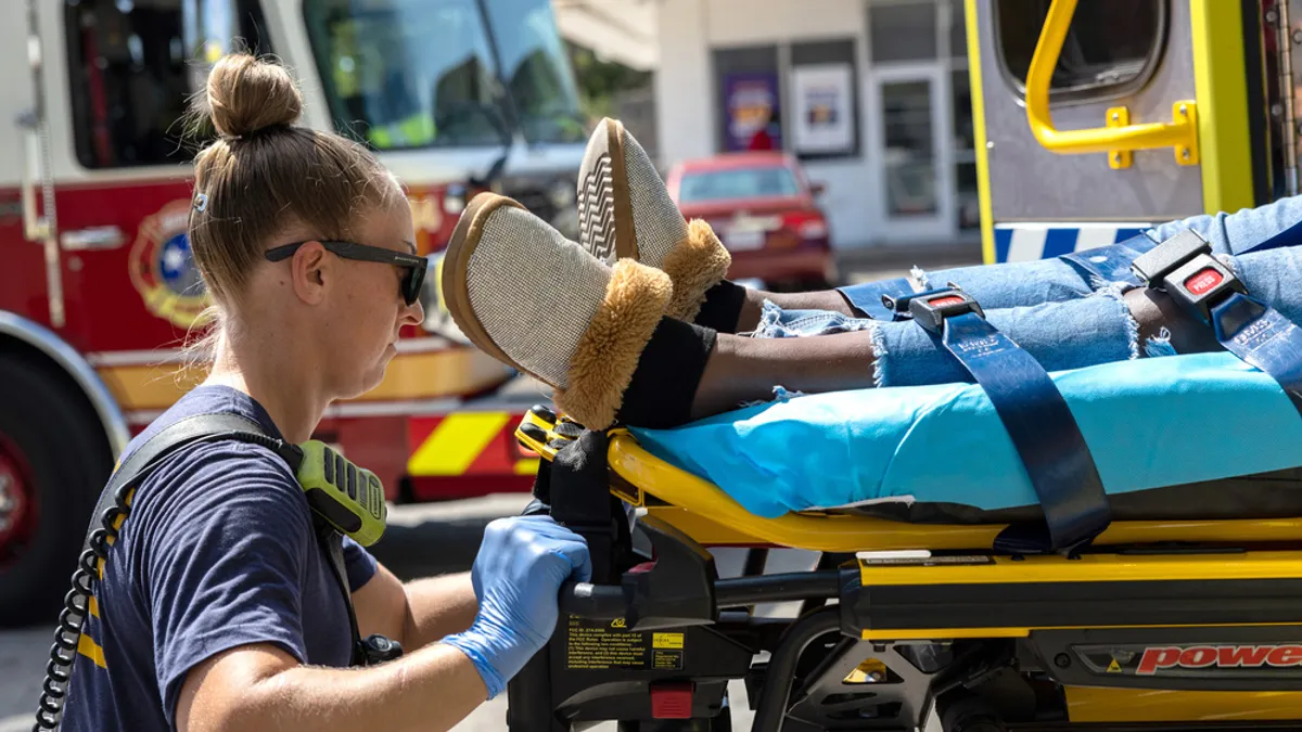 A person pushes a gurney with a person on it into a vehicle