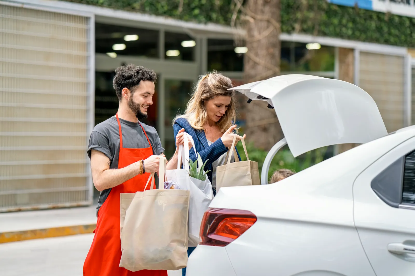 man employee and woman putting grocery bags in the trunk of a car.