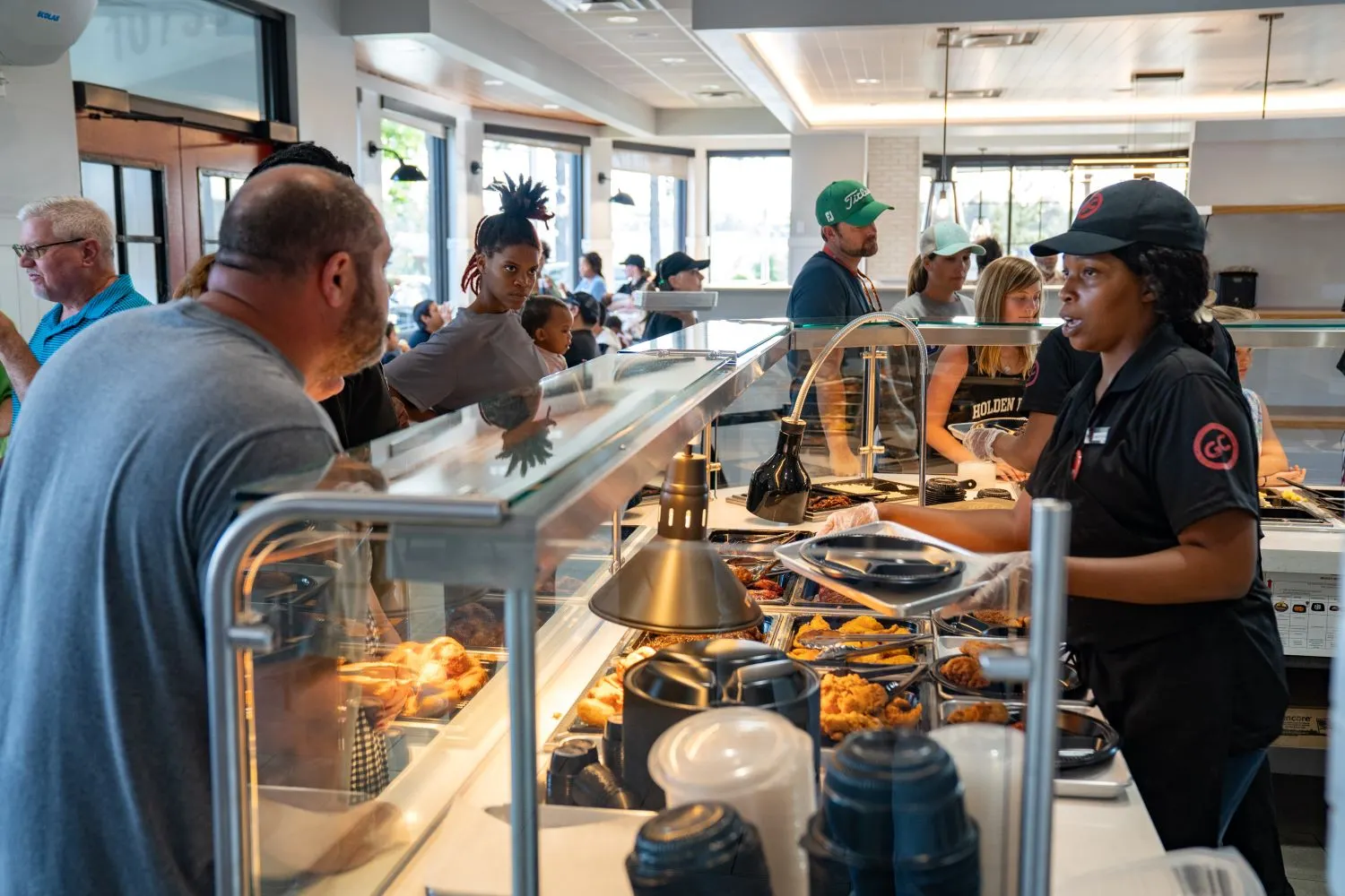 People stand behind a makeline while another person fills a plate with food.