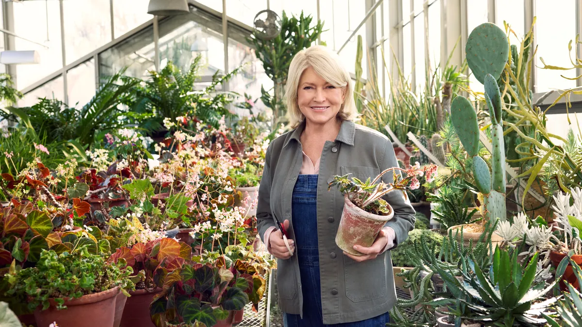 Martha Stewart holding a plant in a greenhouse.