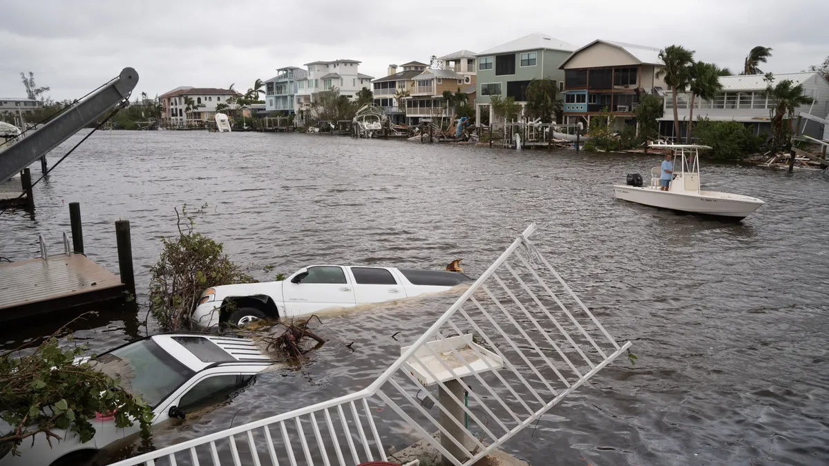 Vehicles float in water as a person mans a boat in the distance assessing damage from Hurricane Ian