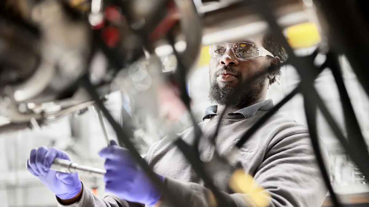 A person wearing protective goggles and blue gloves working in a factory.