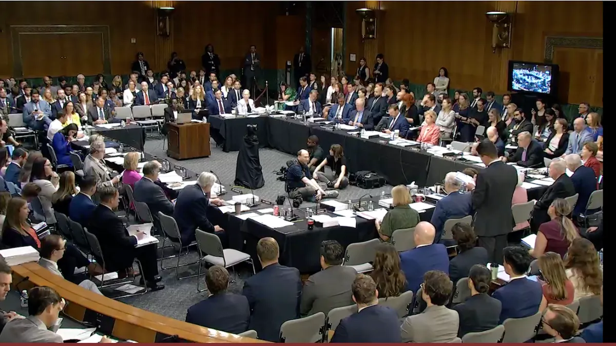 People are sitting at table and in rows of chairs in a large conference rooms