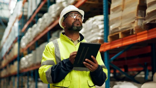 Black man with helmet and tablet at warehouse for distribution industry.