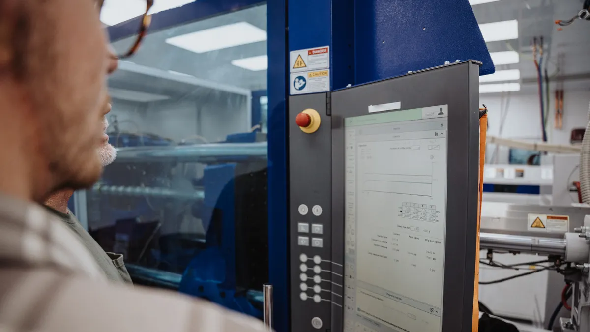 A person looks at a screen on plastic molding equipment