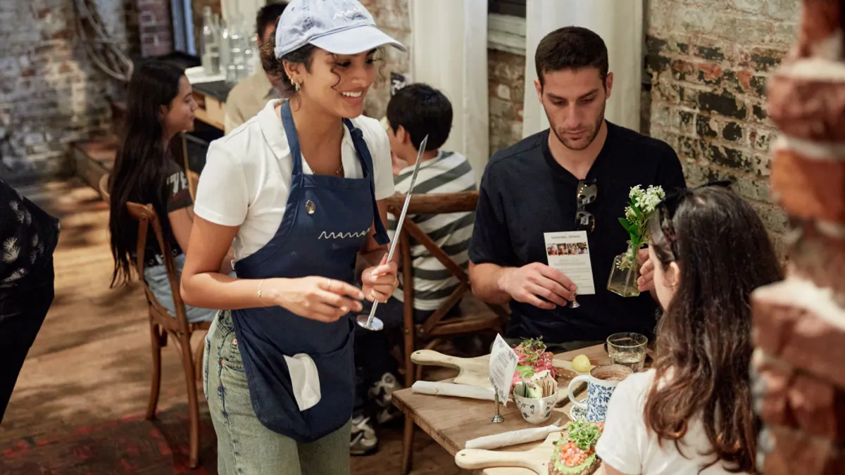A smiling server takes an order from a couple seated at a restaurant table.