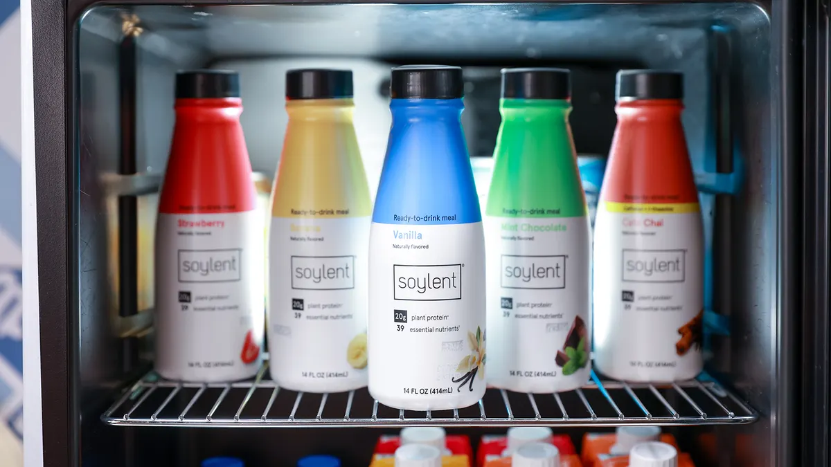 Five bottles of different Soylent flavors sit on the shelf of a mini-fridge.