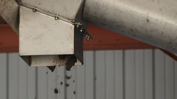 A brown earthy substance falls out of a metal pipe inside a facility.