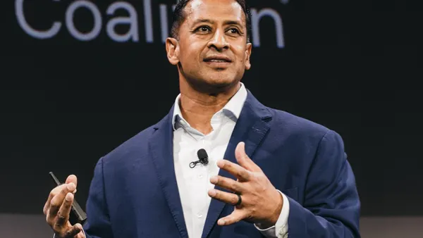 a man in a suit speaking onstage in front of the word "Coalition"