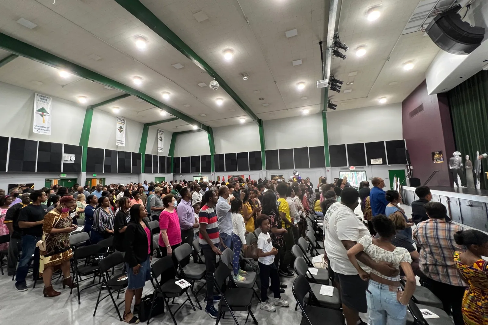 A side camera view of hundreds of people gathered in a school auditorium.