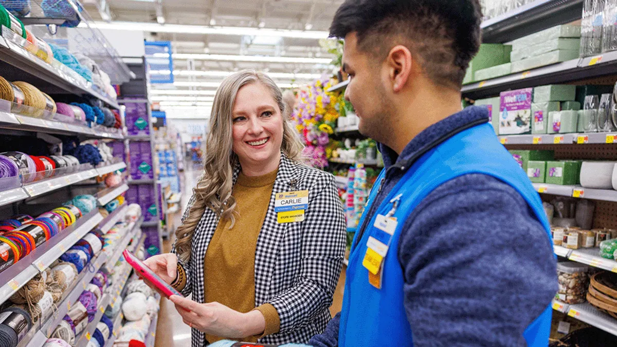 Two Walmart employees inside a store look at a handheld tablet