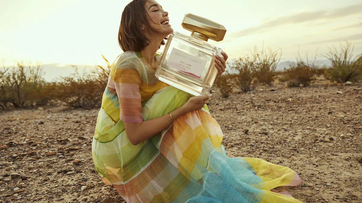 A person holding an oversized bottle of Kendra Scott's Ruby Musk perfume.