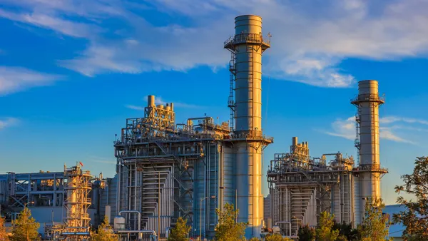 Natural gas fired turbine power plant with it's cooling towers rising into a cloud filled blue sky