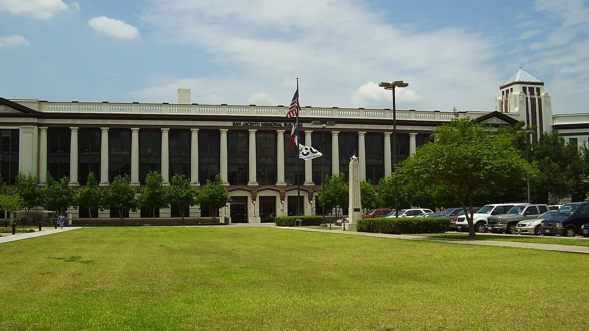 Low, wide building with columns and flags in front, with large lawn in foreground.