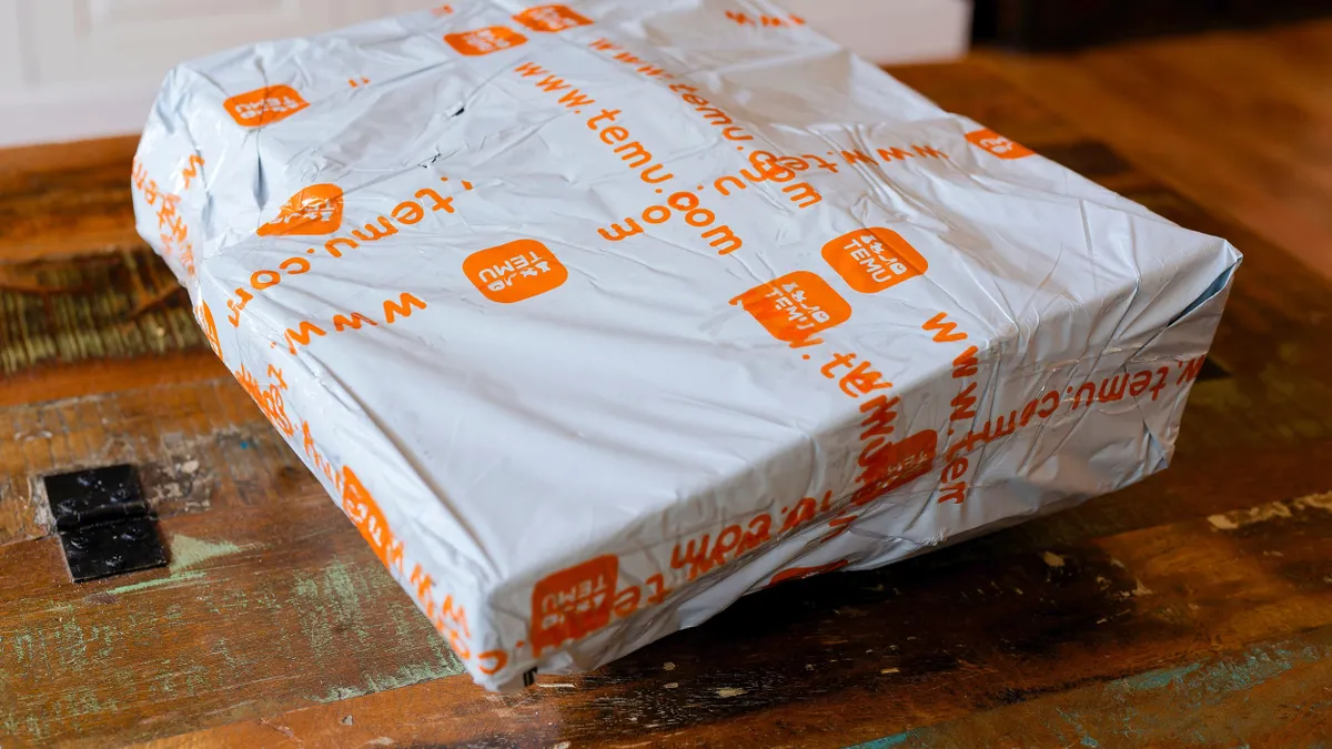 A white plastic shipping package from Temu with orange branding and website text, placed on a rustic wooden table indoors.