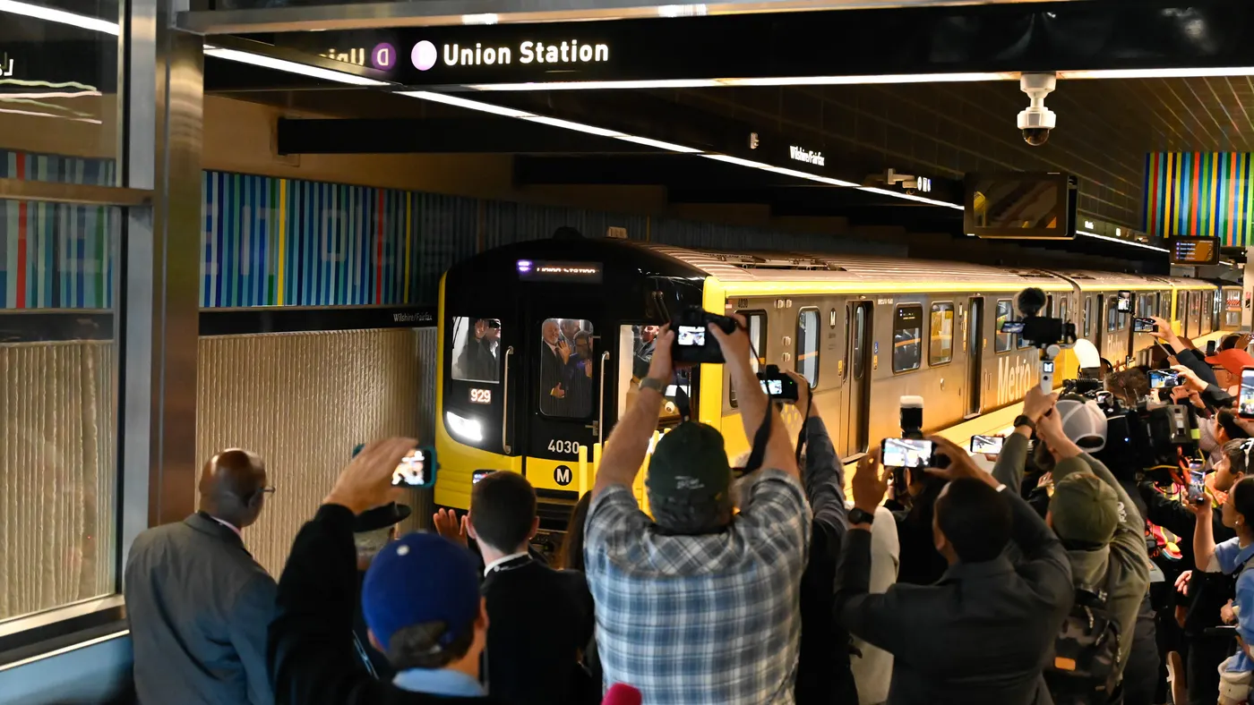 A subway train stops at a station surrounded by photographers and others.