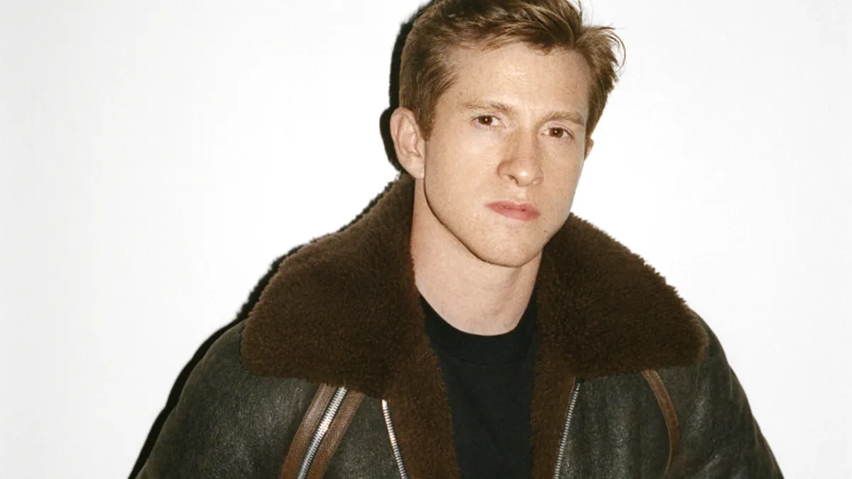 A portrait of fashion designer Daniel Lee wearing a brown leather bomber jacket with brown fur trim.