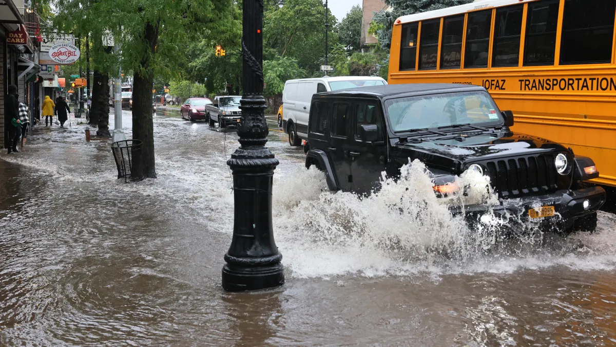 Cars and a yellow bus splash water as they drive through flooded street.