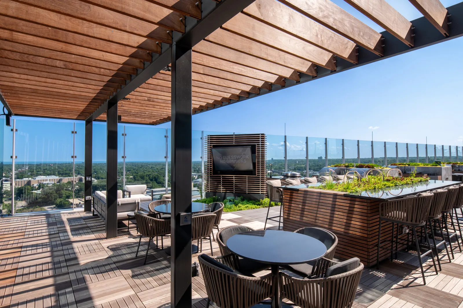 Tables and chairs among greenery on a rooftop.