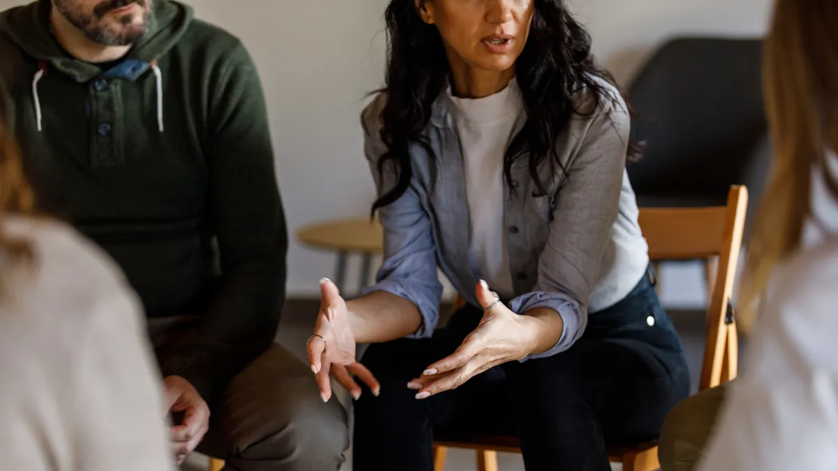 A person sits in a circle of peers, hands extended as they talk.