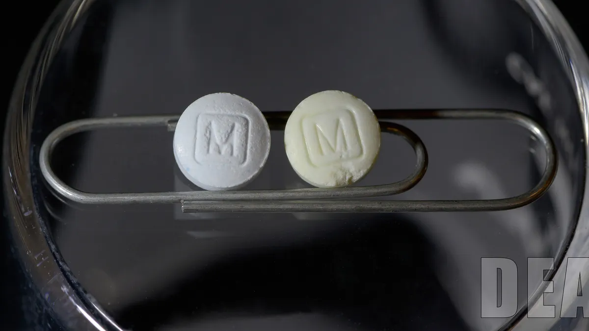 Two pills rest on a paper clip inside a clear lab dish