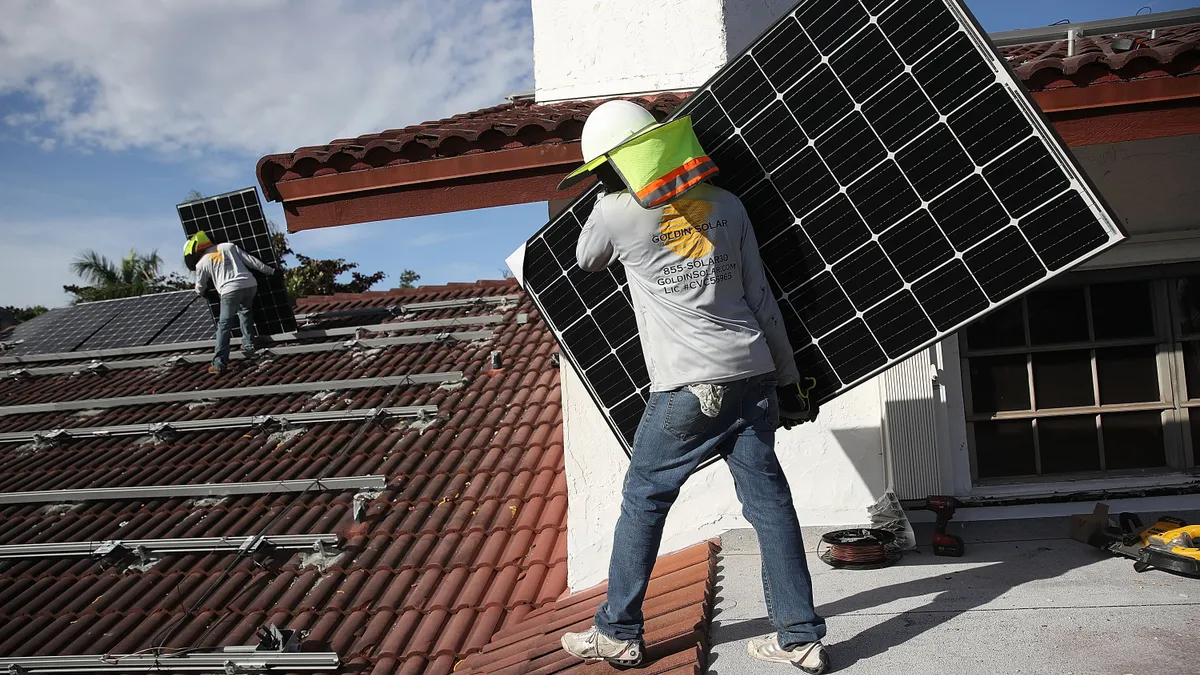 Two workers standing on a roof holding solar panels for installation in a metal framework on the roof.