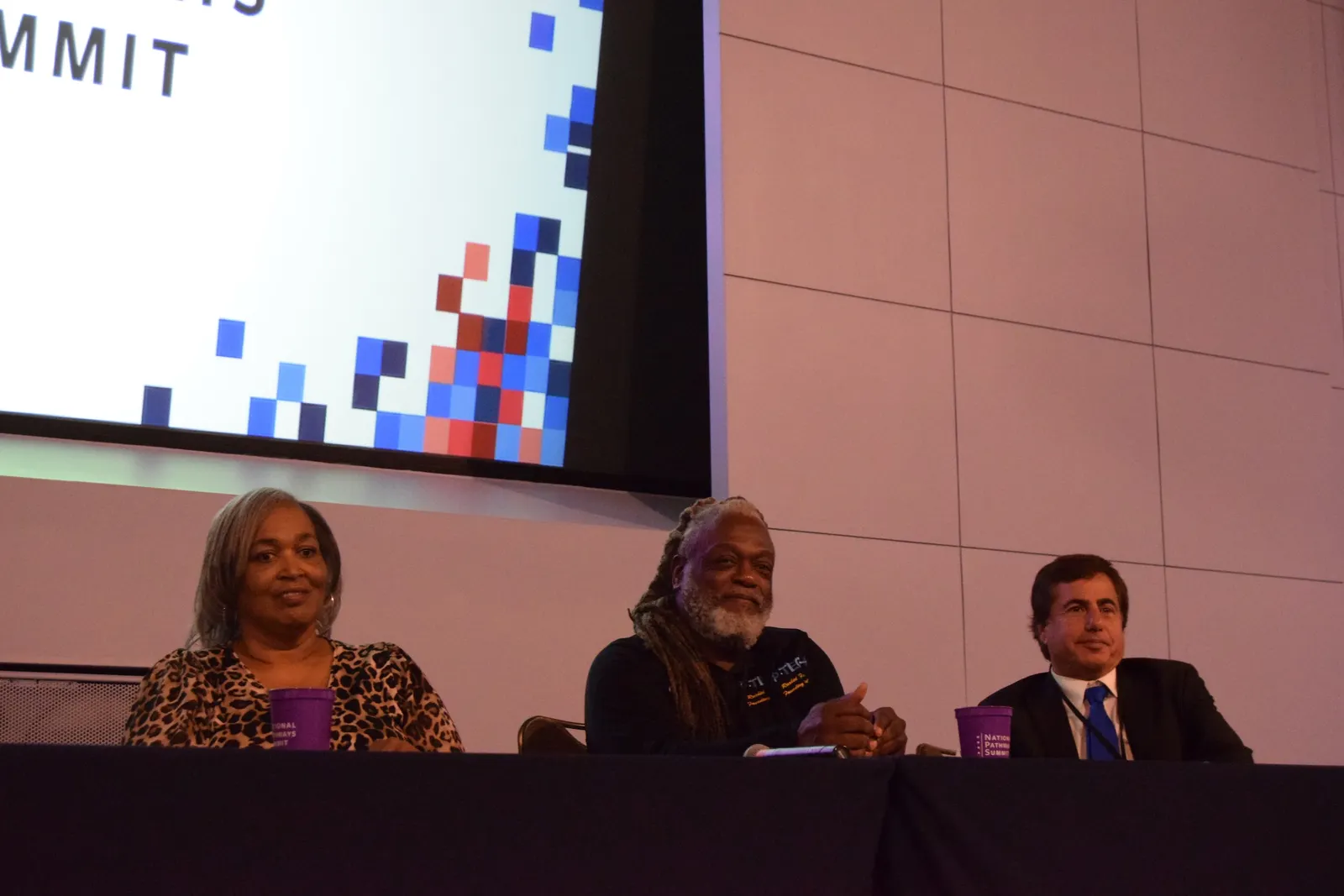 Three people are seated at a table on a stage.