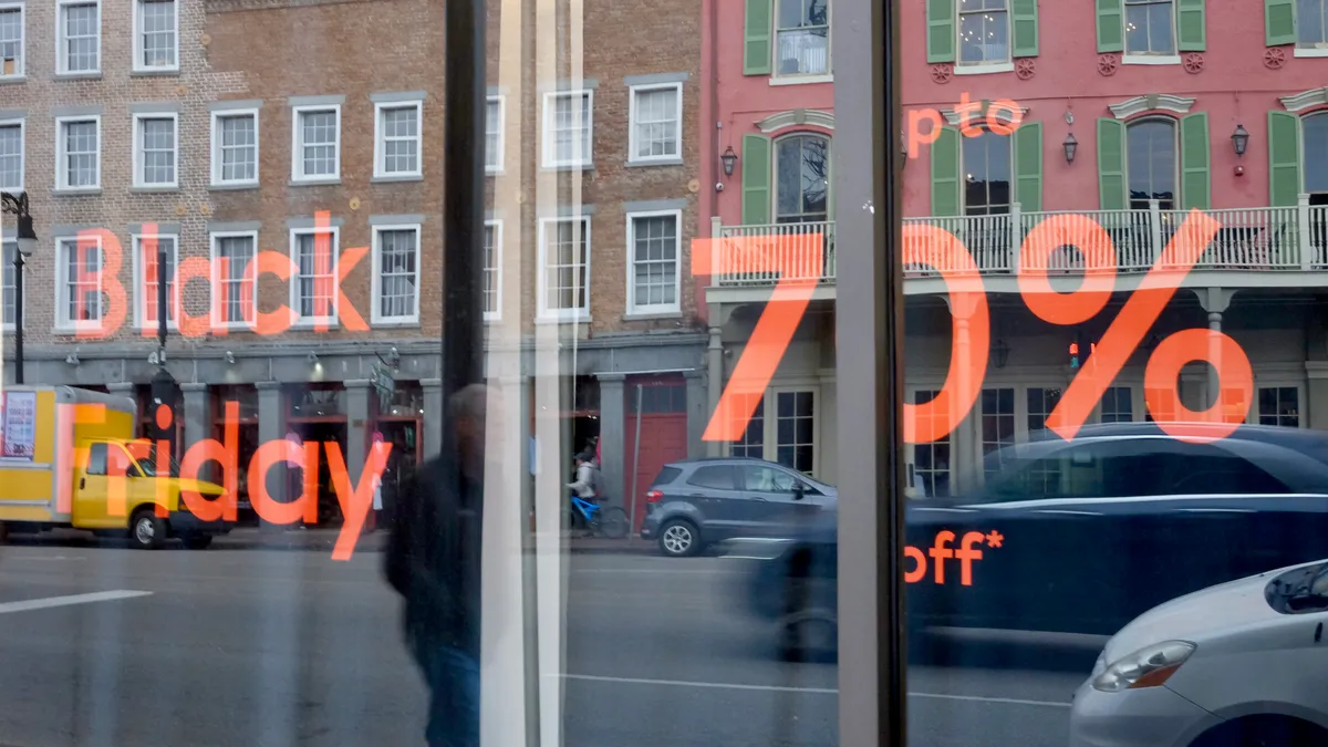 Buildings, cars and a pedestrian are reflected in a store window that says "Black Friday, up to 70% off" in orange letters.