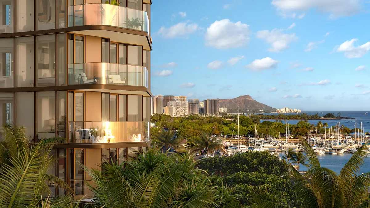 A warm colored building with glass balconies overlooks an ocean.