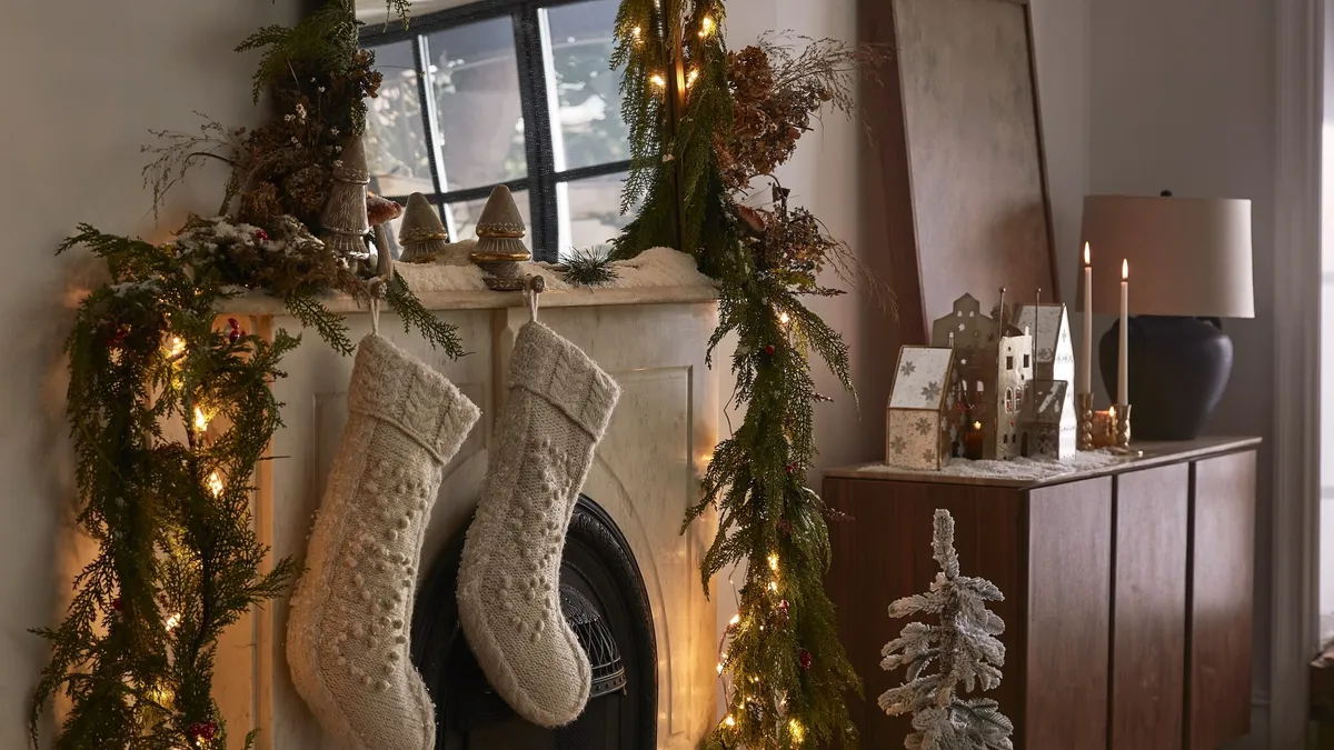 A fireplace with a mirror, stockings, lights and greenery.