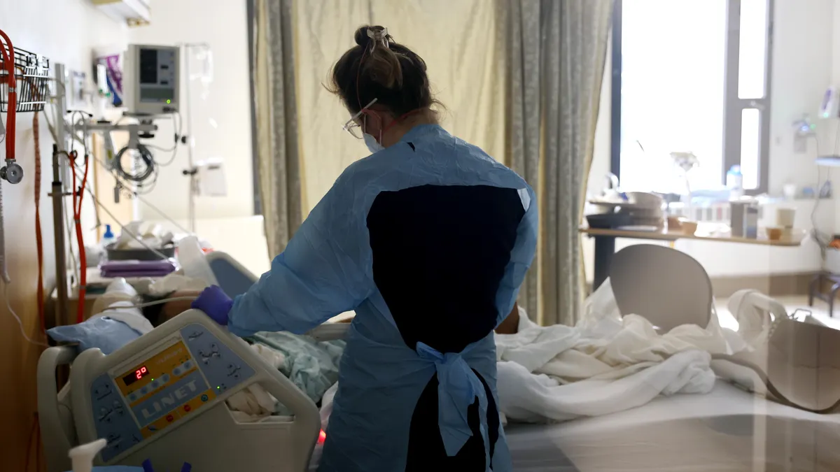 A nurse stands over a patient's bedside in a hospital.