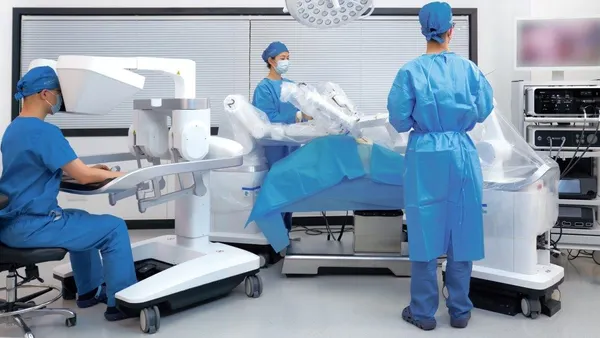 Three clinicians in blue scrubs are shown operating Ronovo Surgical's Carina robotic system.
