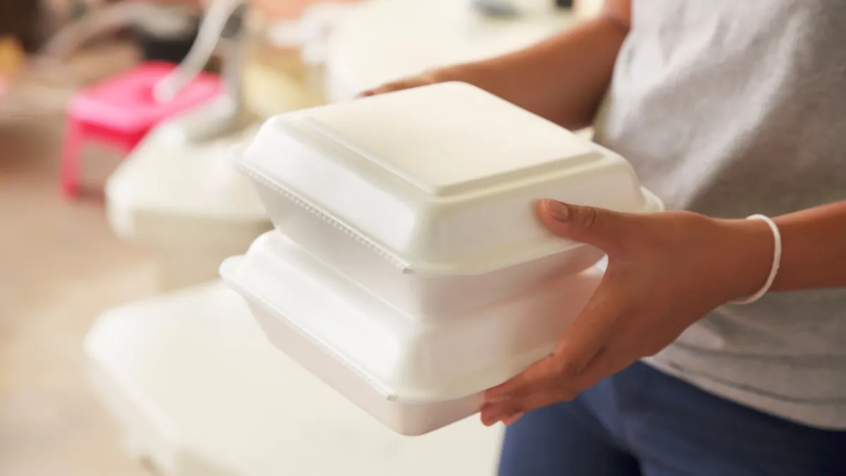 hands hold two stacked foam food service containers