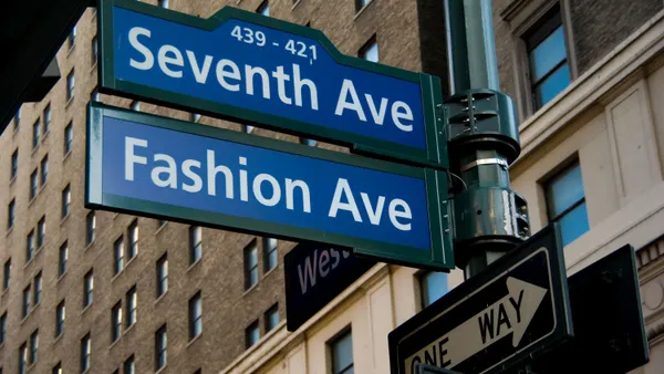 Blue Fashion Avenue street sign above the blue Seventh Avenue street sign in front of a brown brick building.