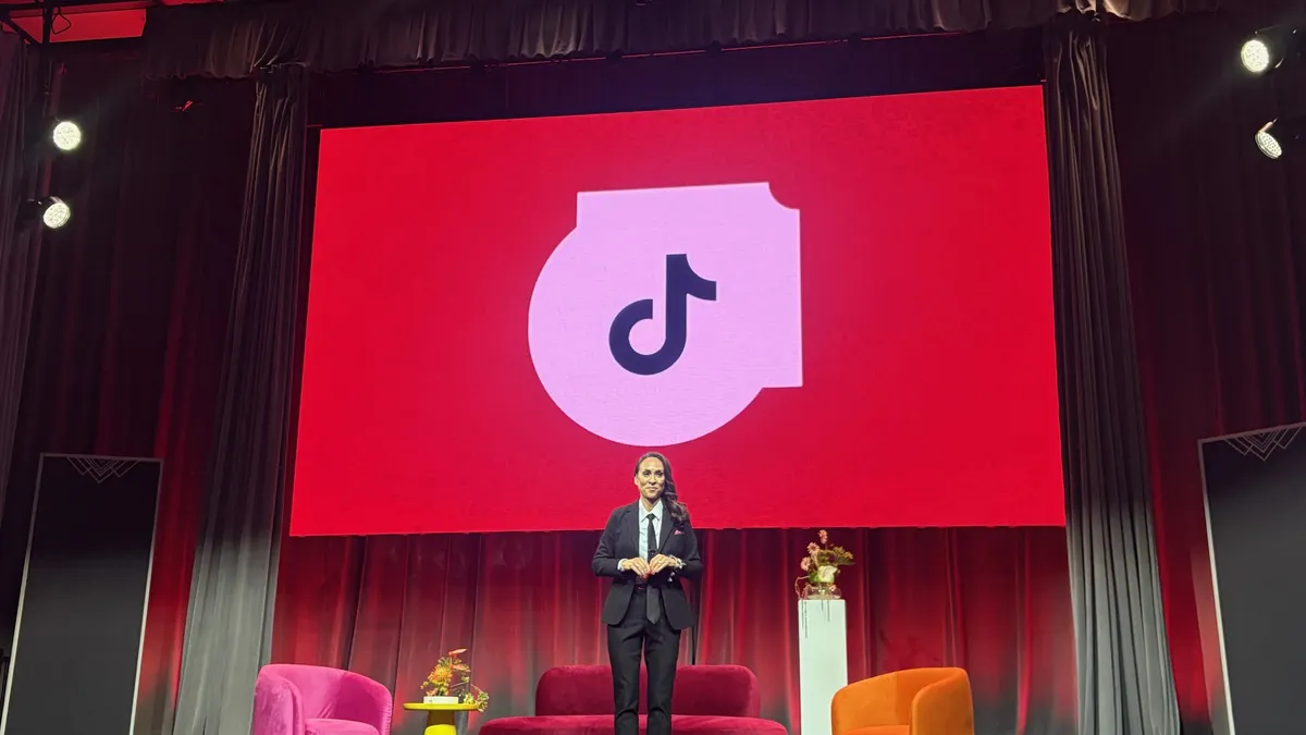 TikTok executive Khartoon Weiss stands on a stage in front of a screen showing the app's logo on a red background.