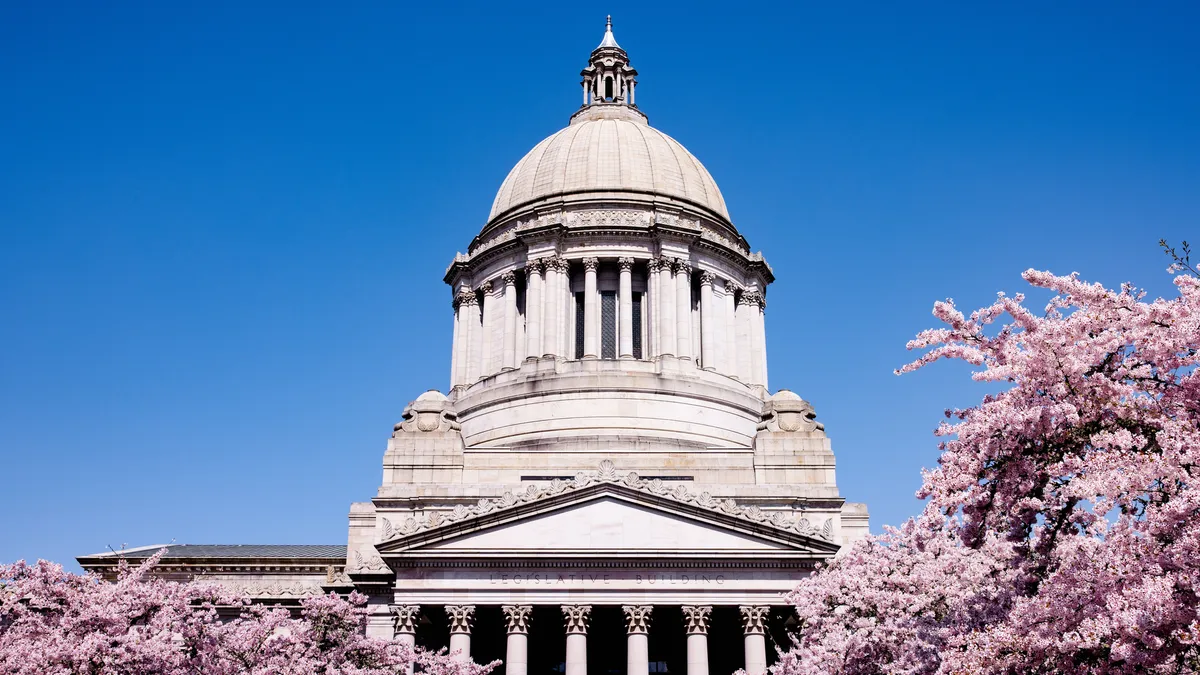 A view of the state capitol building in Olympia, Washington, with pink flowering cherry trees bordering the stone architecture.